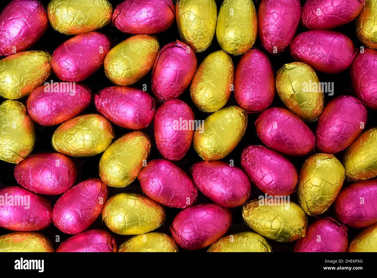 Pile ou groupe de plusieurs couleurs et différentes tailles d'oeufs de pâques au chocolat enveloppés de papier d'aluminium coloré en jaune, or et rose. Banque D'Images