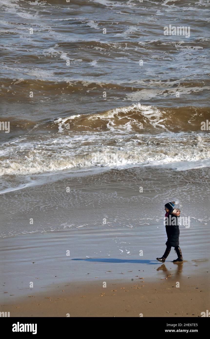 femme solitaire socialement distancée marchant le long de la ligne d'eau à mundesley norfolk en angleterre Banque D'Images