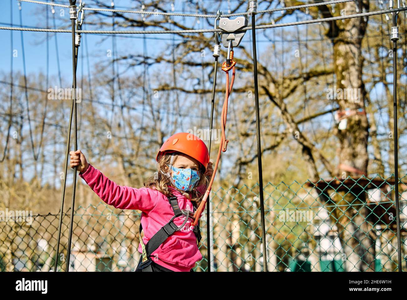 Petite fille avec des protections pratiquant l'escalade entre les arbres avec des cordes et des filets Banque D'Images