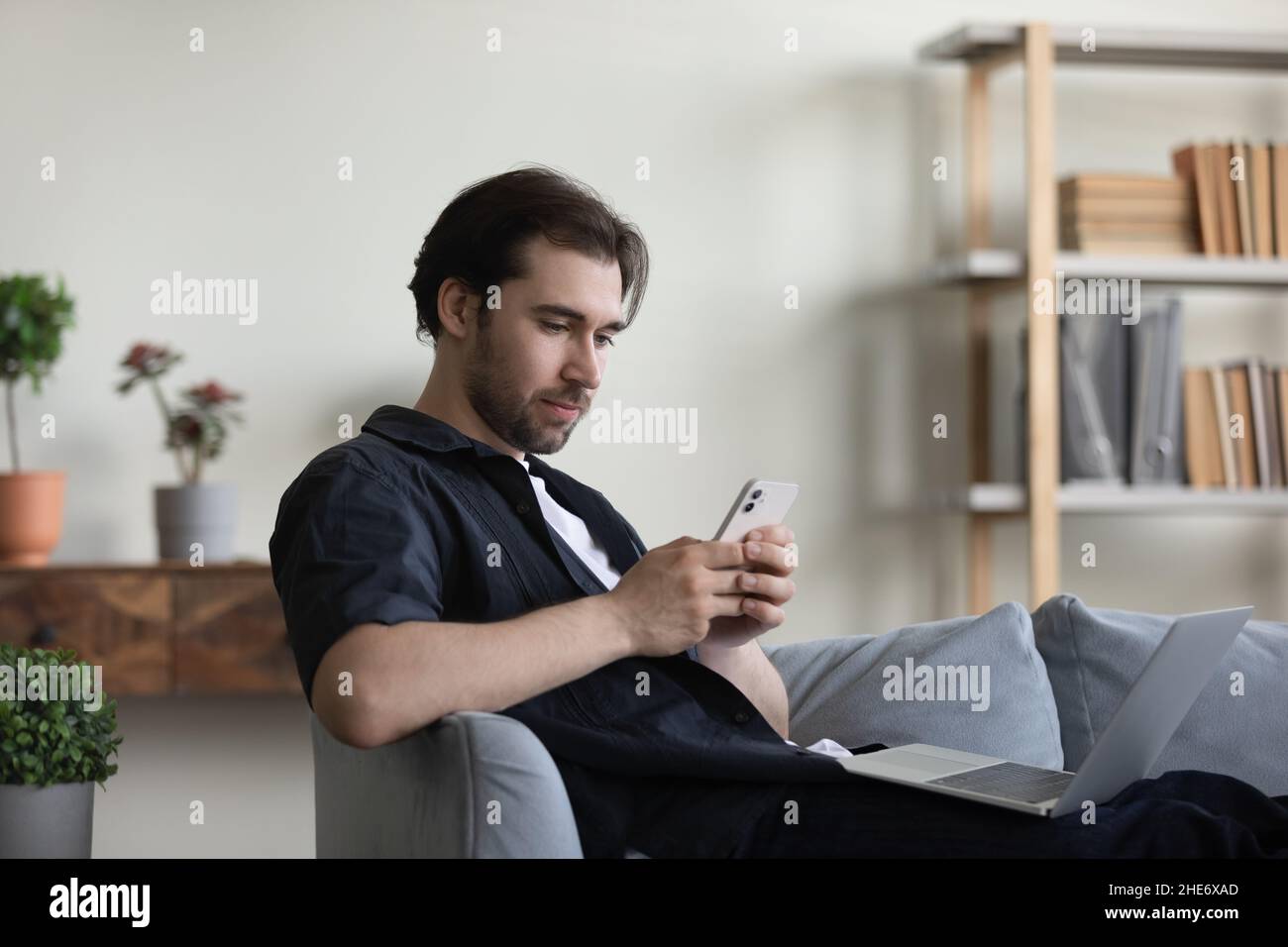 Joyeux jeune homme détendu utilisant le téléphone portable à la maison. Banque D'Images