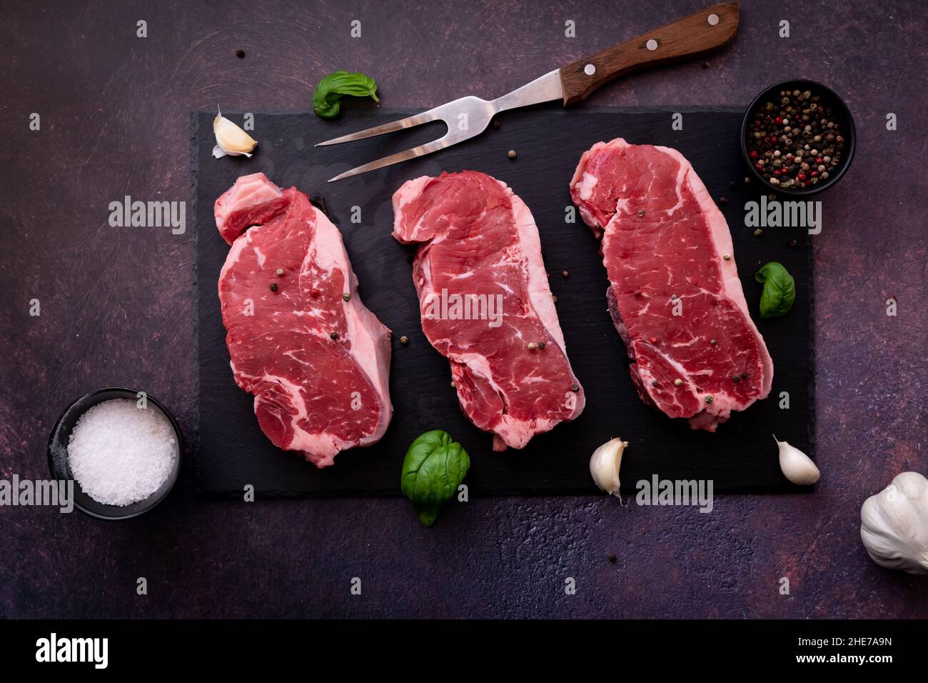 Vue de dessus en bas des steaks de striploin crus sur un tableau d'ardoise noir, prêt pour le gril Banque D'Images