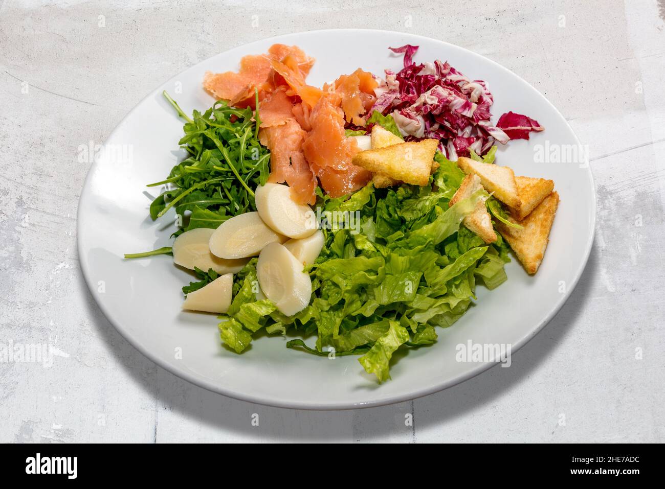 Salade mixte avec saumon fumé, laitue, roquette, chicorée rouge, coeur de palmier et croûtons.Dans un plat blanc dans la vue de dessus Banque D'Images