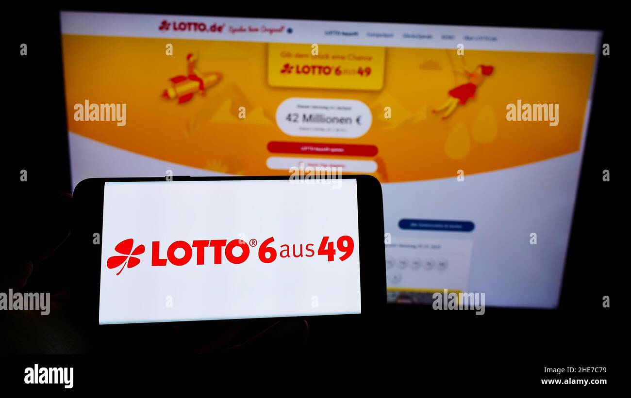 Personne tenant un téléphone portable avec le logo de la loterie allemande Deutsche Lotto- und Totoblock à l'écran en face de la page web d'affaires.Mise au point sur l'affichage du téléphone. Banque D'Images