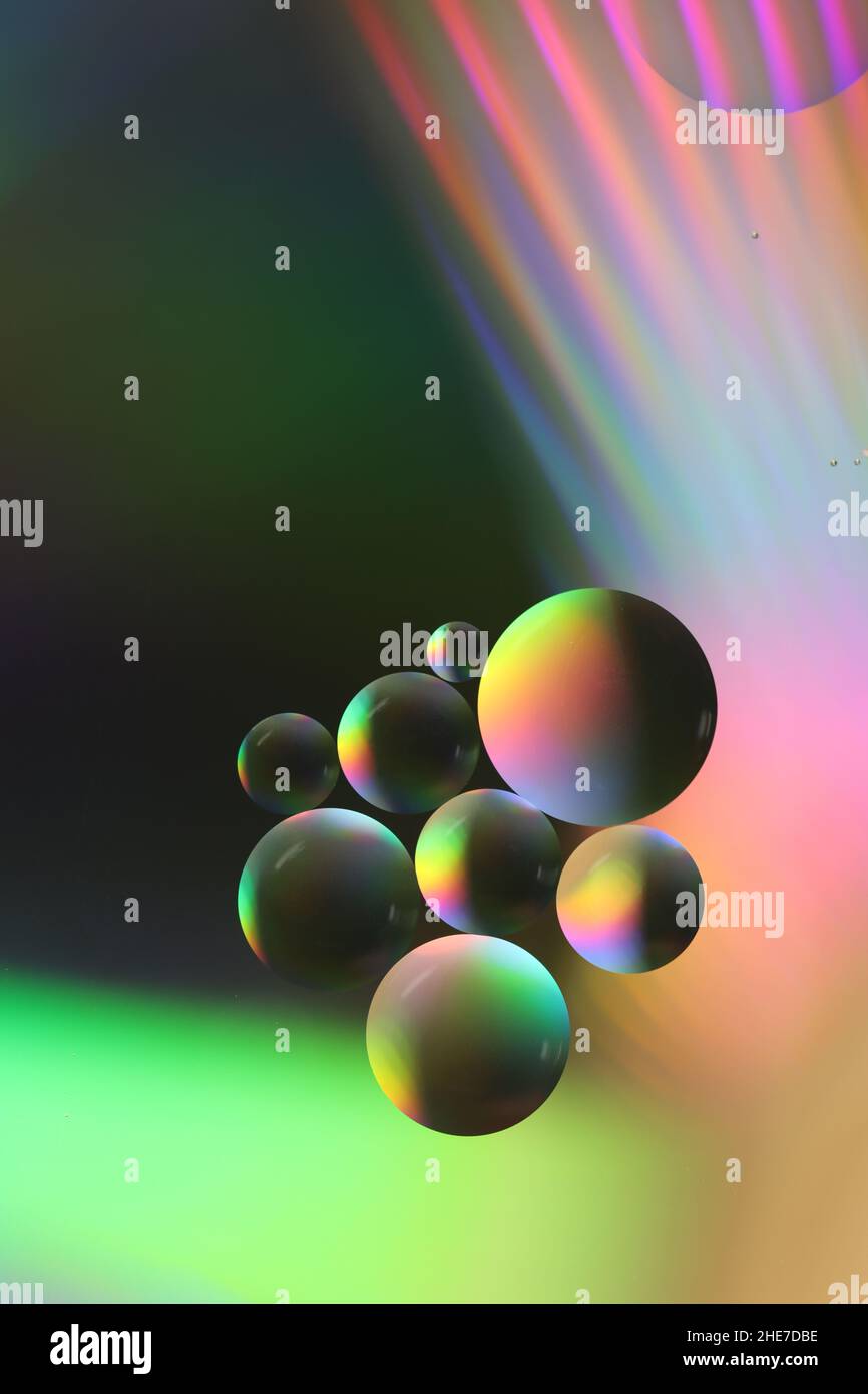 gros plan de petites et grandes gouttelettes d'huile flottant sur une surface d'eau et illuminées par une lumière colorée Banque D'Images