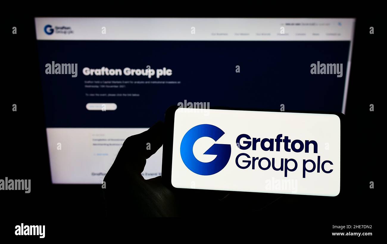 Personne tenant un smartphone avec le logo de la société marchande de constructeurs Grafton Group plc à l'écran devant le site Web.Mise au point sur l'affichage du téléphone. Banque D'Images