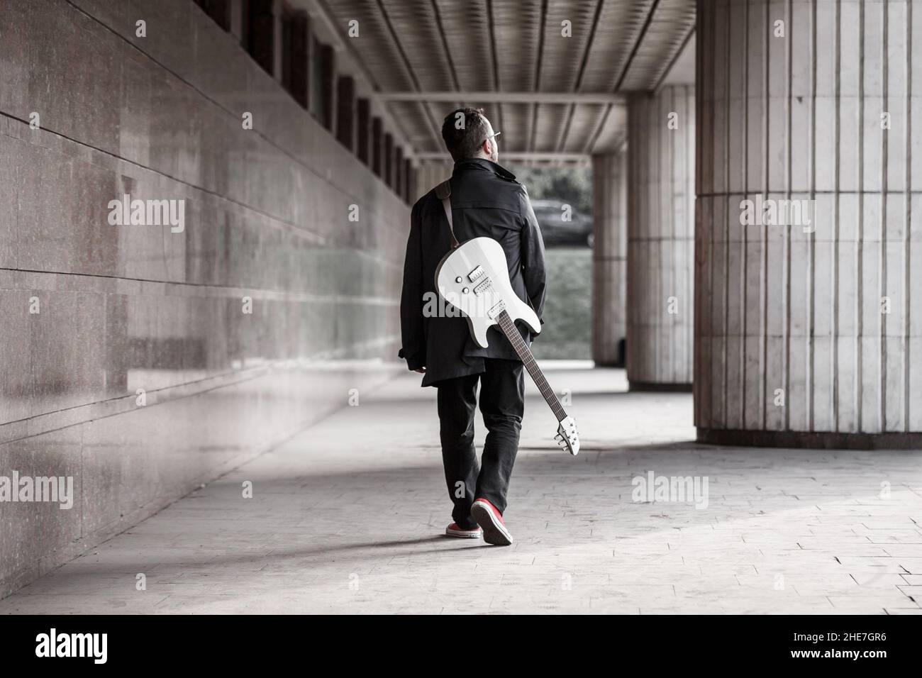 Homme en noir avec une barbe avec guitare électrique sur un emplacement urbain en plein air.Guitare, solo et musique de rue Banque D'Images