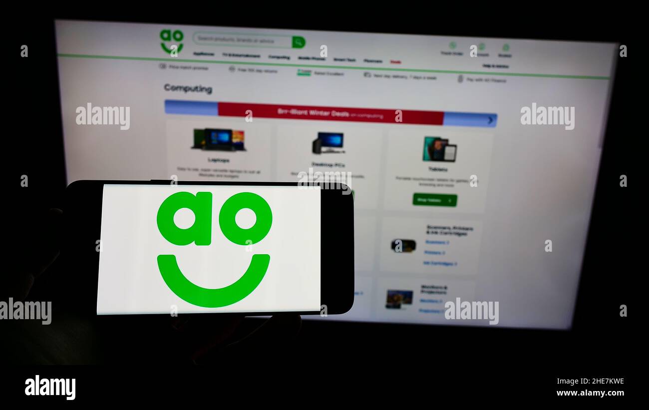 Personne tenant un smartphone avec le logo de la société britannique de vente en ligne AO World plc à l'écran devant le site Web.Mise au point sur l'affichage du téléphone. Banque D'Images Personne tenant un smartphone avec le logo de la société britannique de vente en ligne AO World plc à l'écran devant le site Web.Mise au point sur l'affichage du téléphone. Banque D'Images