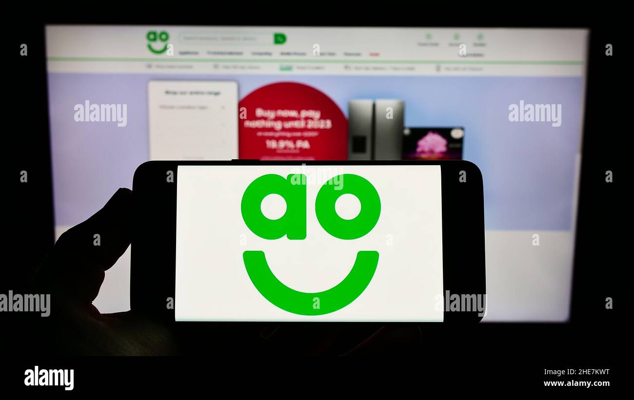 Personne tenant un téléphone portable avec le logo de la société britannique de vente au détail en ligne AO World plc à l'écran en face de la page Web d'affaires.Mise au point sur l'affichage du téléphone. Banque D'Images Personne tenant un téléphone portable avec le logo de la société britannique de vente au détail en ligne AO World plc à l'écran en face de la page Web d'affaires.Mise au point sur l'affichage du téléphone. Banque D'Images