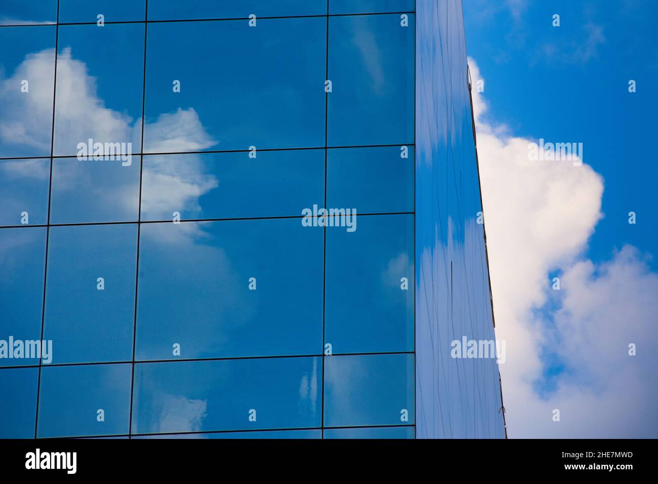 Réflexions de ciel bleu et de nuages blancs sur le verre des fenêtres d'un immeuble de bureaux. Banque D'Images