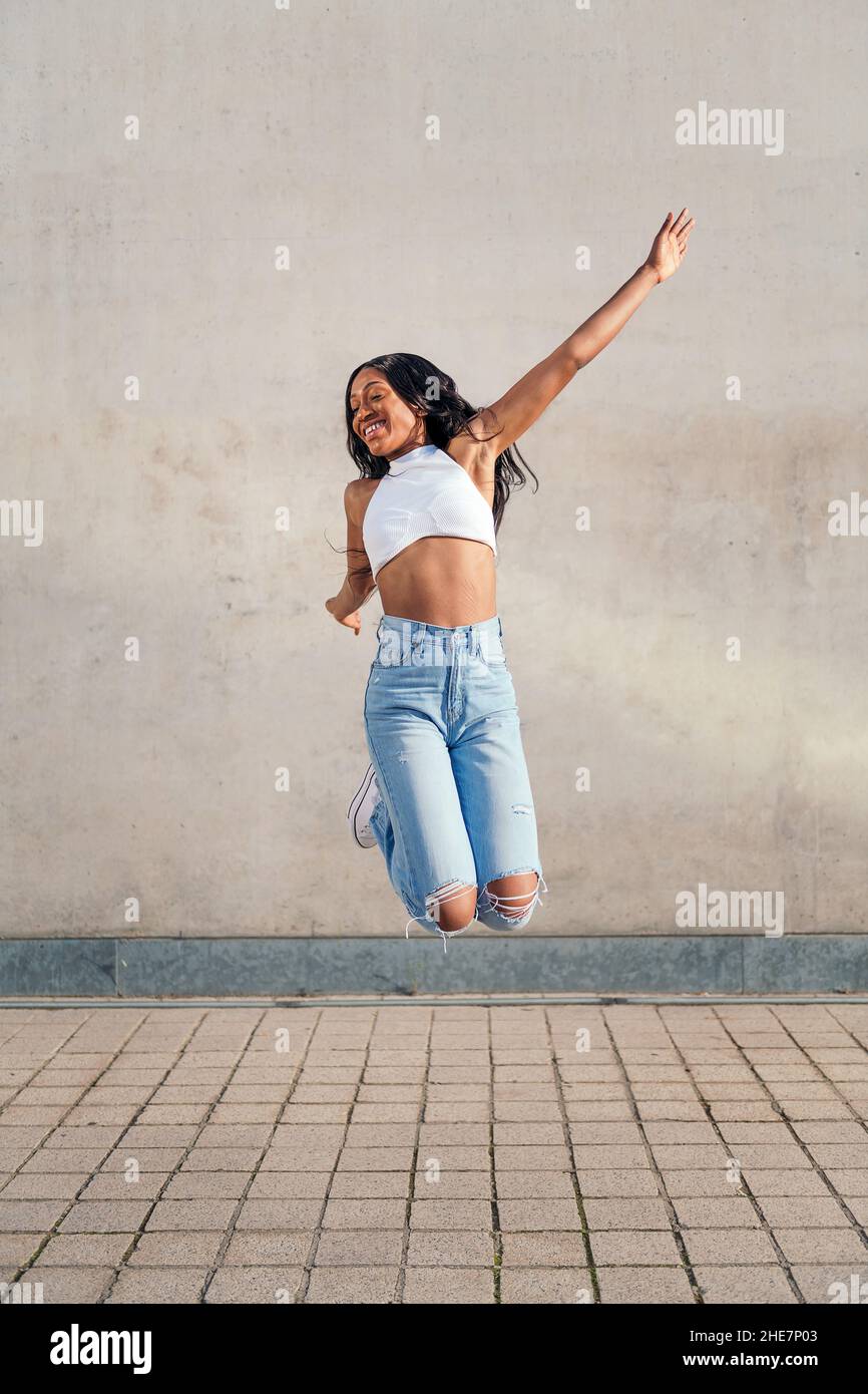 une jeune femme africaine saute heureuse et souriante avec un mur de béton gris en arrière-plan, le concept de jeunesse et de diversité raciale, l'espace de copie pour le texte Banque D'Images