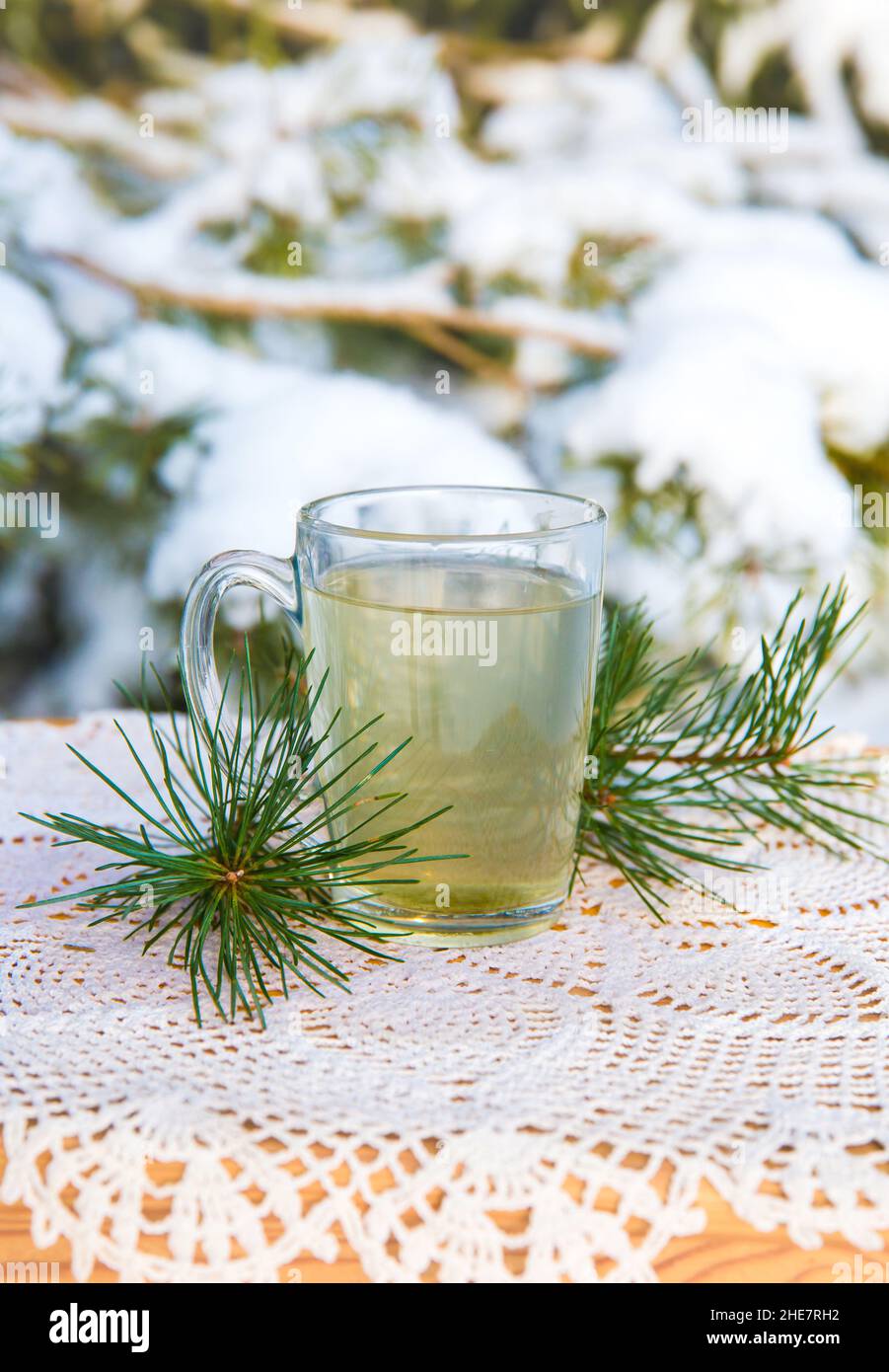 Infusion de thé à aiguille de pin chaud dans une tasse de thé en verre transparent sur la table.Pins enneigés en arrière-plan, en plein air par temps froid d'hiver. Banque D'Images