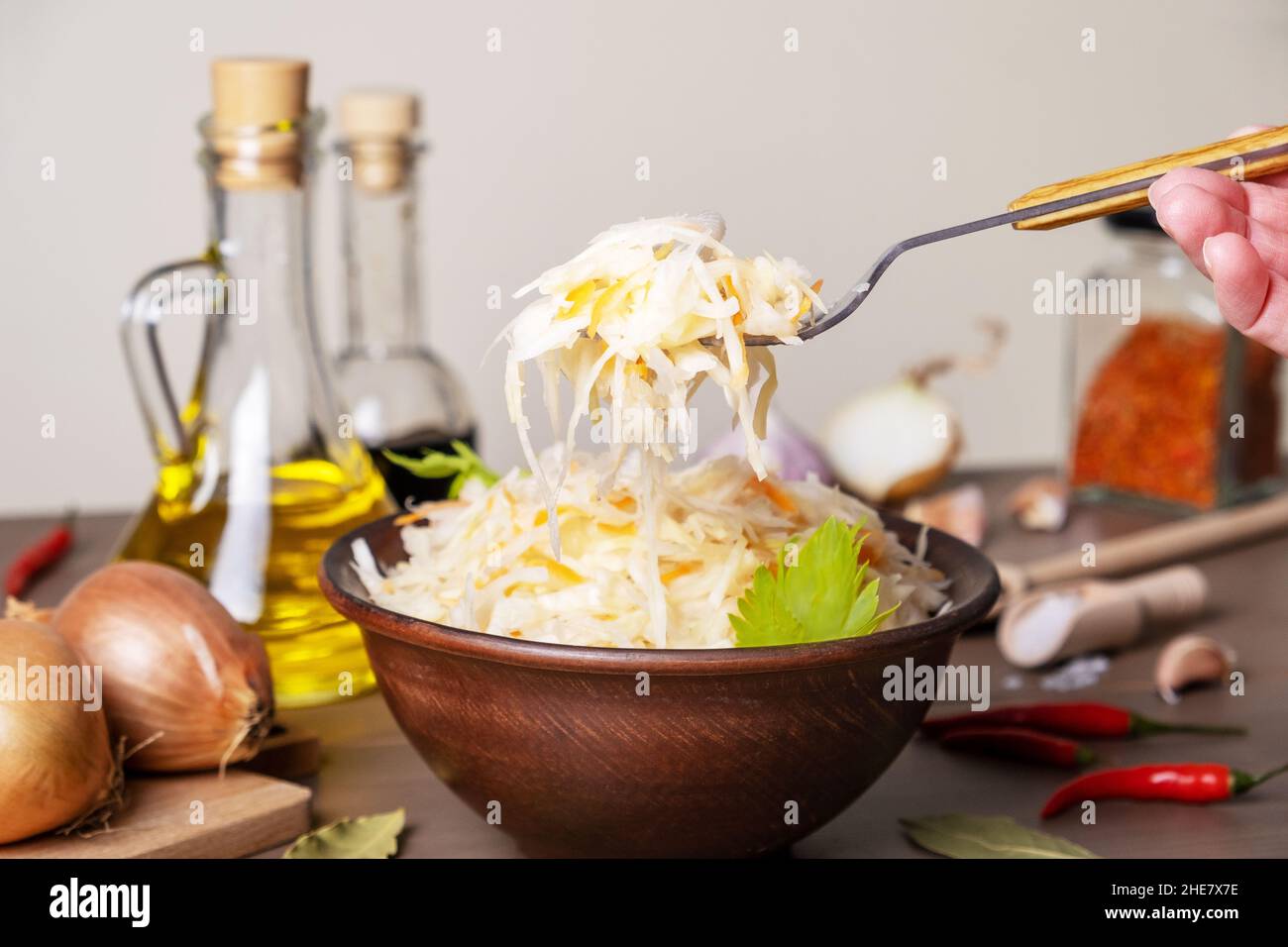 Chou fermenté dans un bol en céramique sur la table avec des épices et des ingrédients.La main tient la fourchette avec la salade.Nourriture saine, cuisine traditionnelle russe. Banque D'Images
