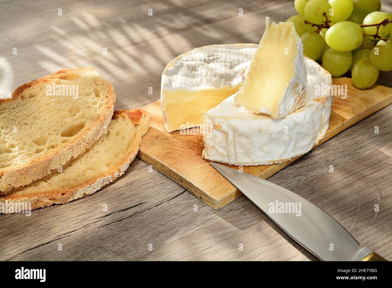 Camembert français de Normandie servi sur une planche à découper en bois avec des raisins et des tranches de pain. Banque D'Images