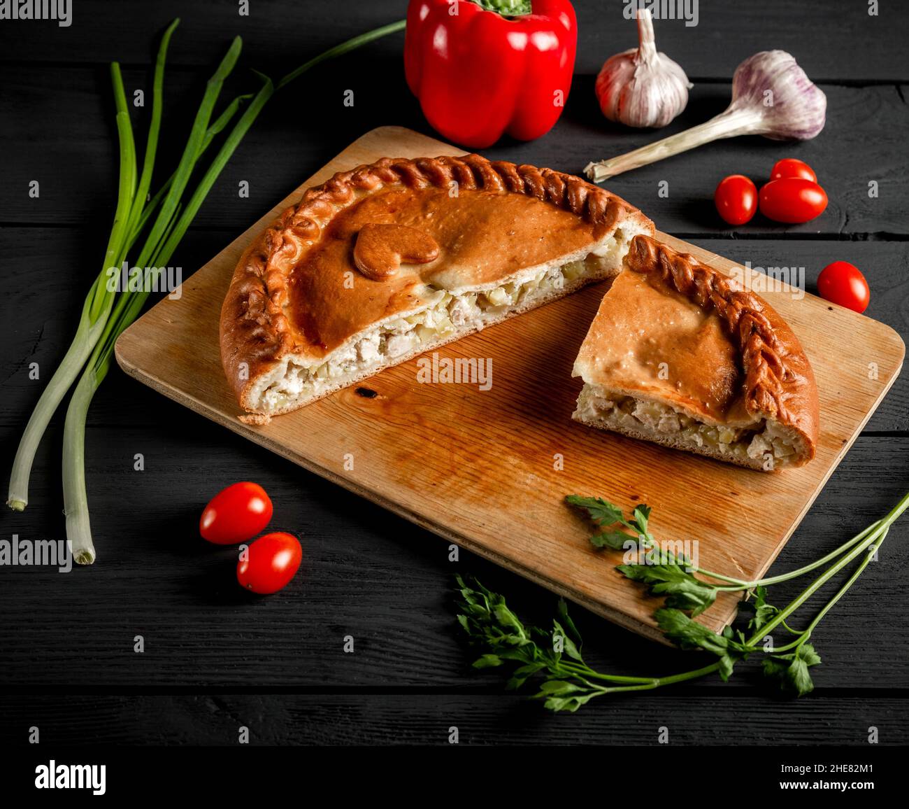 Tarte en tranches avec de la viande et des pommes de terre sur une planche à découper.Composition sur fond noir avec ingrédients. Banque D'Images