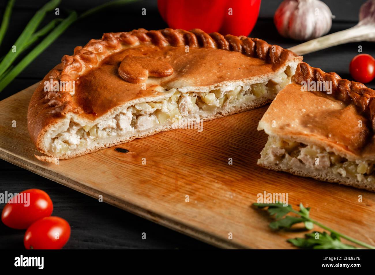 Tarte en tranches avec de la viande et des pommes de terre sur une planche à découper.Composition sur fond noir avec ingrédients. Banque D'Images