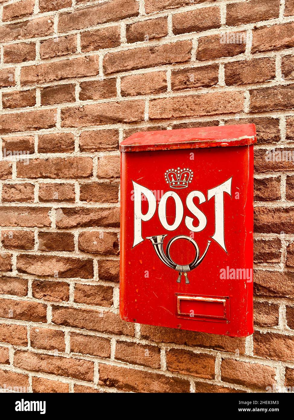 Ancienne boîte de poteau en métal rouge vif traditionnel avec le mot et l'image de corne sur l'avant attaché à la façade de la maison, vieux mur de brique de la maison.Service postal p Banque D'Images