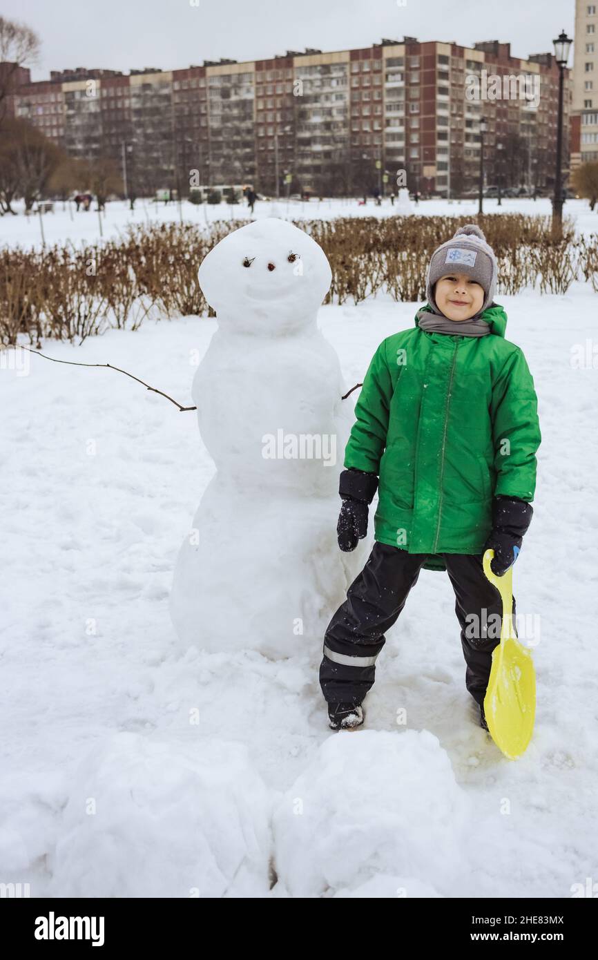 Joyeux garçon debout près du bonhomme de neige dans le parc d'hiver Banque D'Images