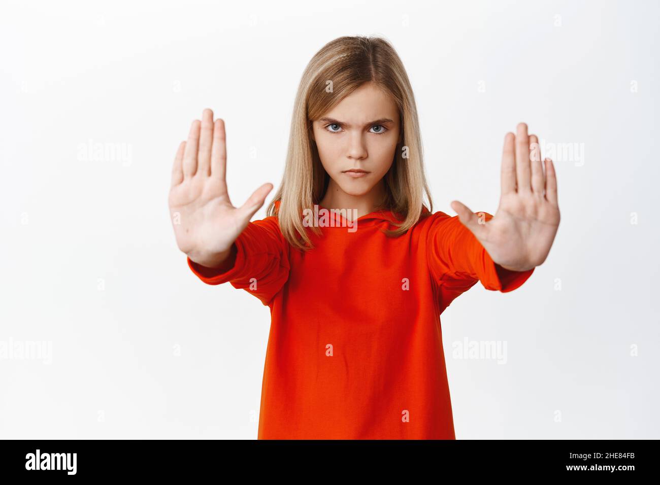 Petite fille sérieuse montrant stop, interdiction tabou geste, étendant les bras et bloquant smth mauvais, rejetant, se tenant sur fond blanc Banque D'Images