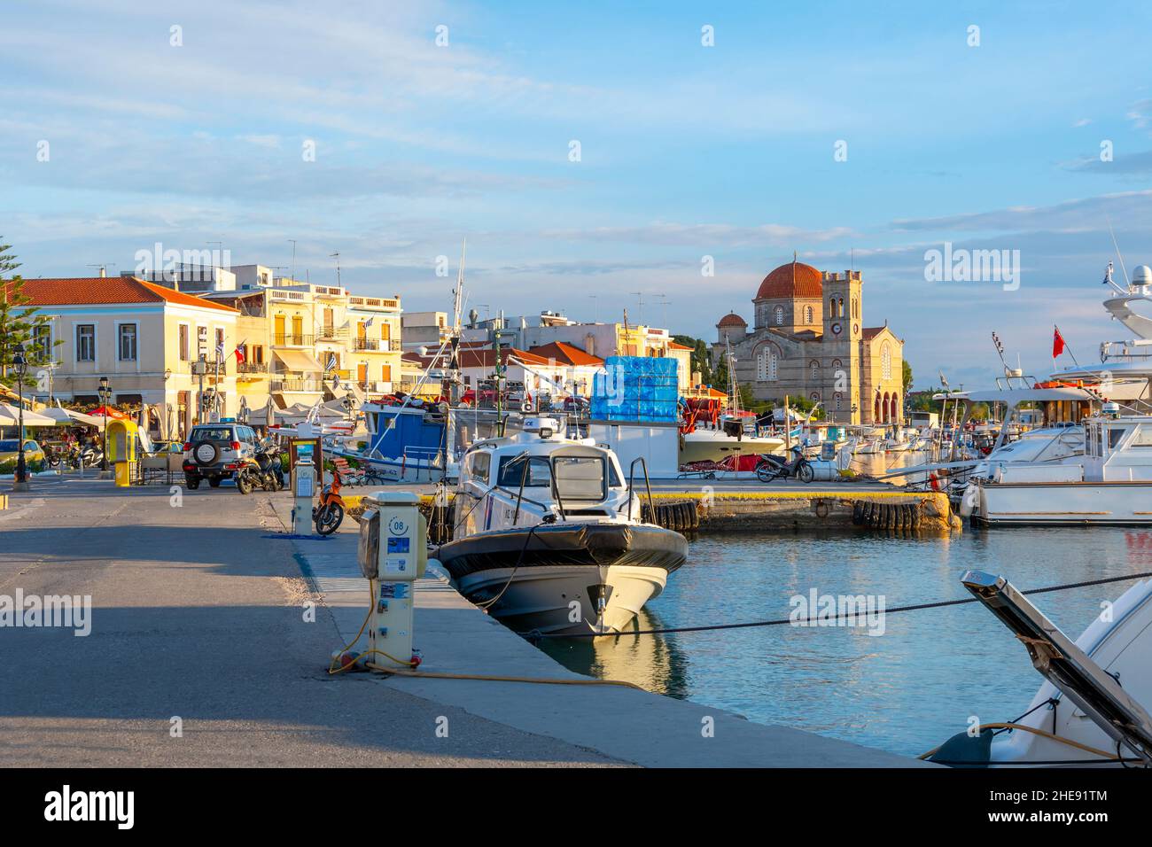 La promenade de bord de mer des magasins et l'église de Panagitsa au port du village de pêcheurs d'Aegina, Grèce au coucher du soleil. Banque D'Images