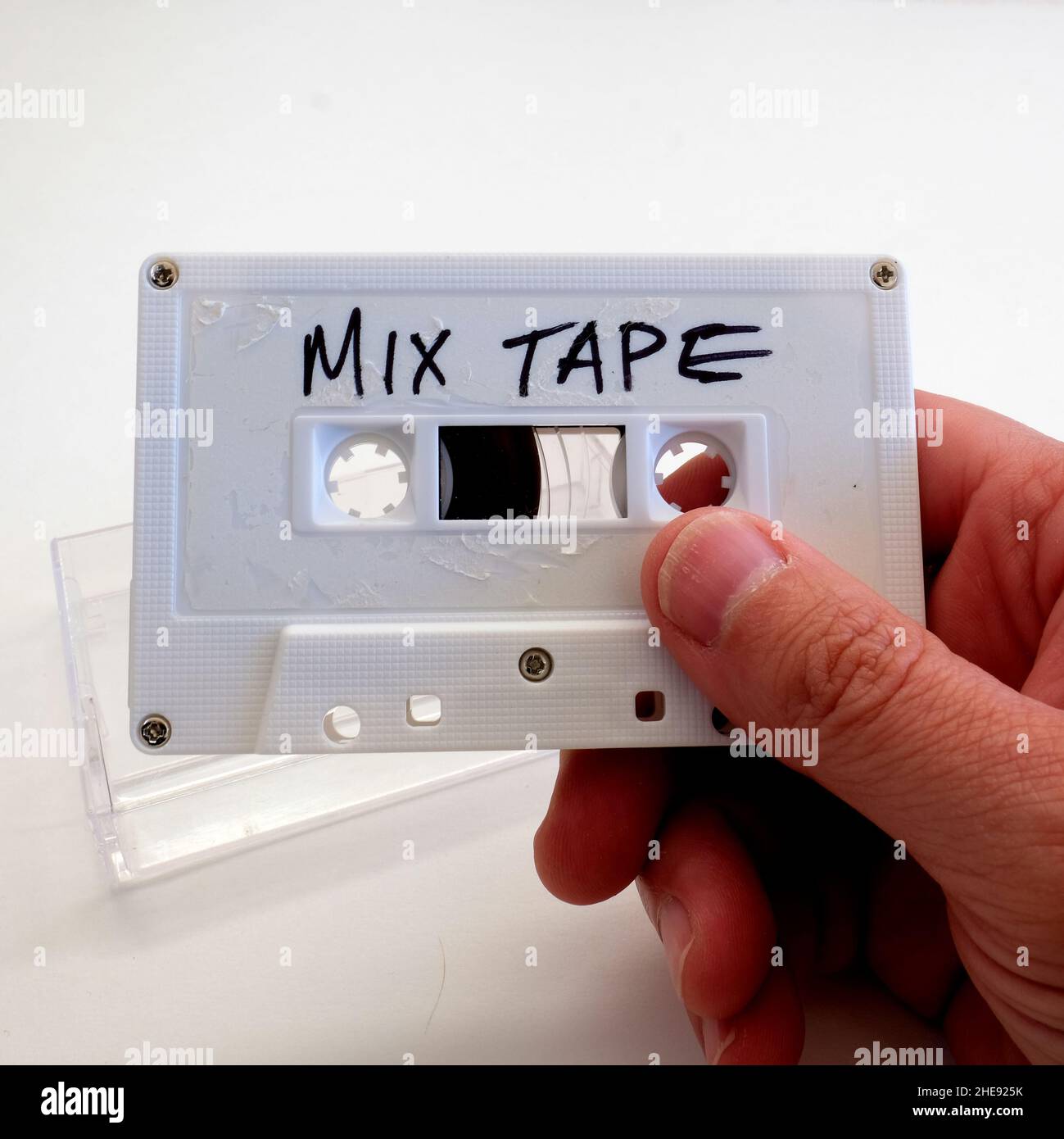 Main de l'homme tenant une cassette blanche avec les mots BANDE MIXTE écrit en main lettres de script et boîtier en plastique transparent en arrière-plan. Banque D'Images