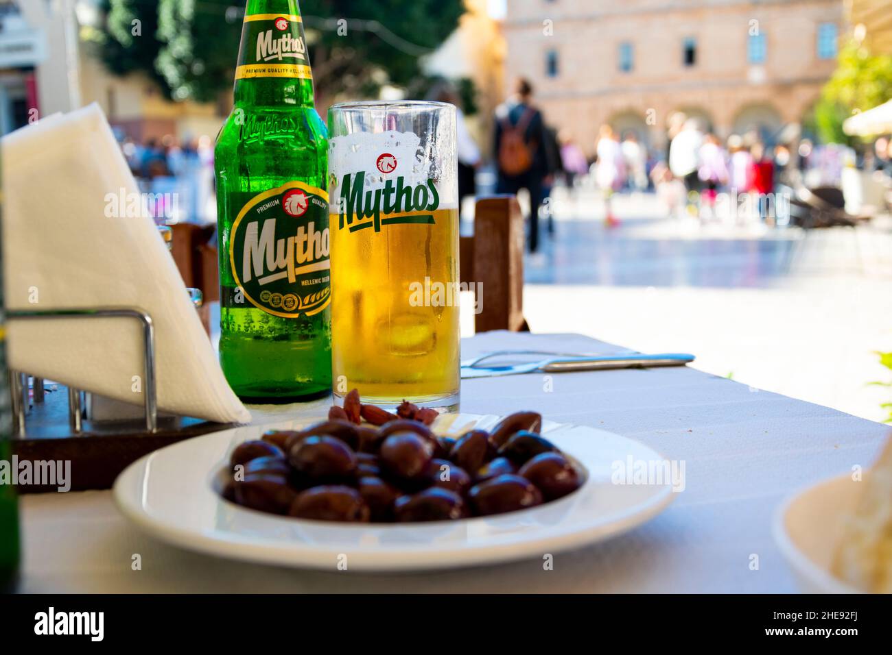 Vue depuis une table extérieure avec des olives et une bouteille et un verre de Mythos Beer par une journée ensoleillée dans la ville grecque. Banque D'Images