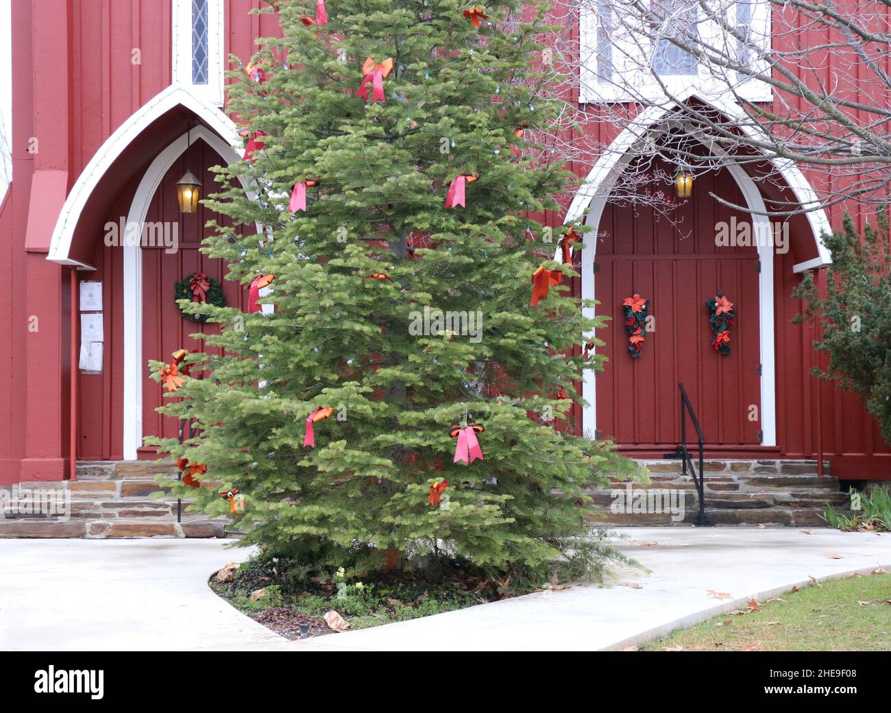 Deux portes rouges d'une église historique de Sonora, CA.Une couronne de Noël festive sur les portes et un arbre de Noël décoré accueillent la saison de l'Avent. Banque D'Images