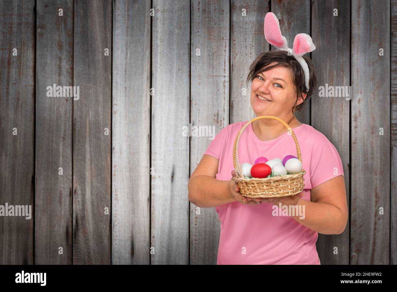 Femme dans les oreilles de lapin avec des œufs de Pâques dans un panier sur fond de bois Banque D'Images