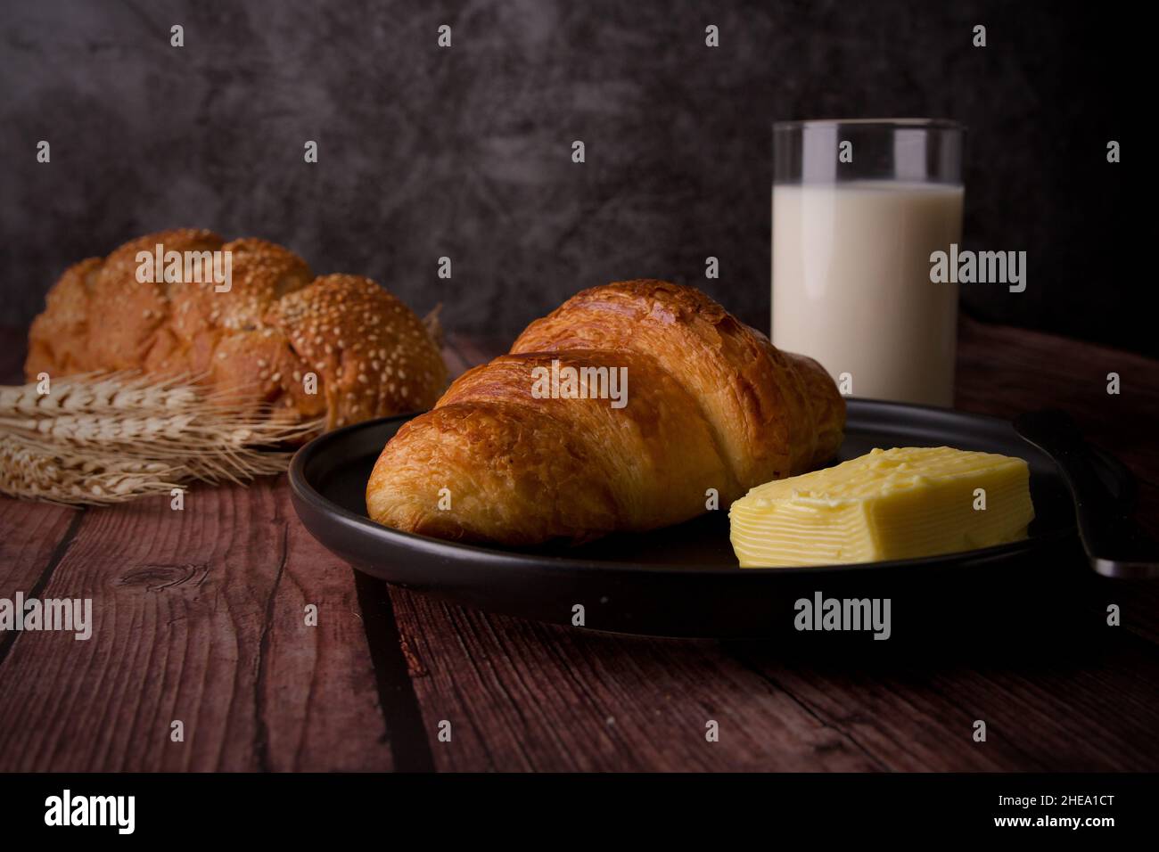 Délicieux croissant de petit déjeuner avec du beurre sur une table en bois avec du lait en verre. Banque D'Images