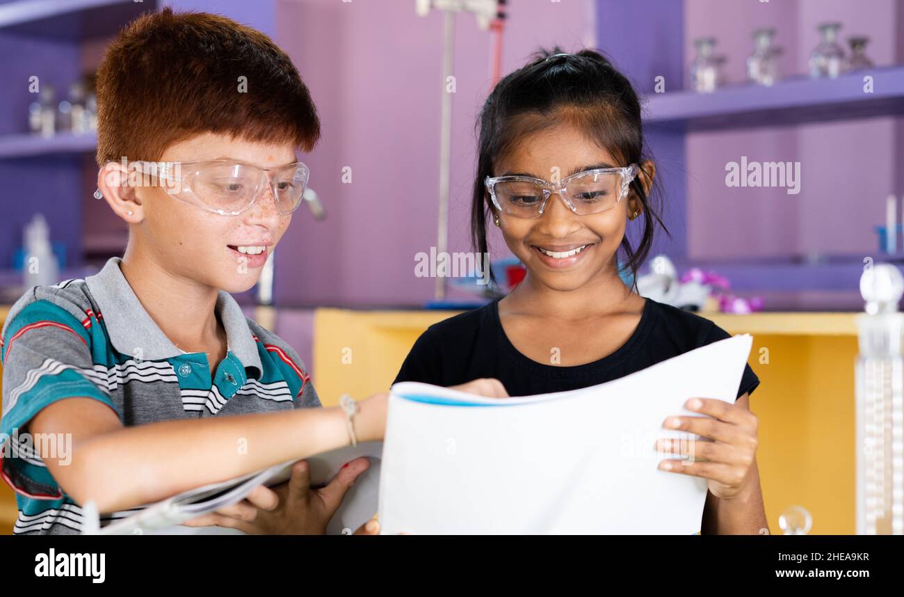 Deux enfants multi-ethniques discutant de laboratoire d'expérience scientifique mon manuel d'utilisateur de voir - concPET de l'amitié d'enfance, l'apprentissage de nouvelles compétences et Banque D'Images