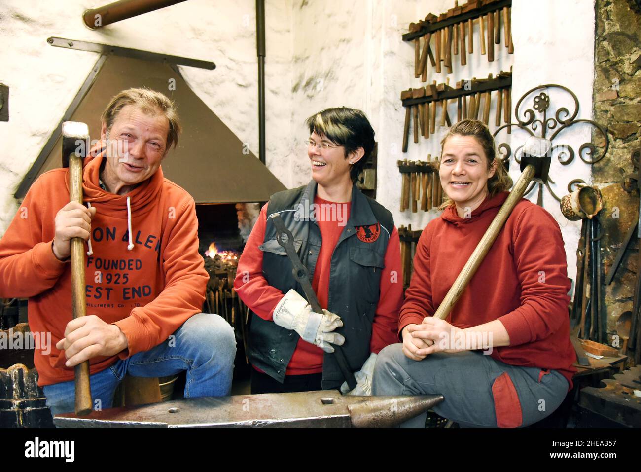 16 décembre 2021, Saxe, Leipzig: Rire, le forgeron d'art Andreas Althammer se tient devant le feu de forge à l'enclume avec ses filles, le maître métallurgiste et chef actuel de la forge, Elisabeth Althammer-Kluge (M) et le forgeron de métal et compagnon Claudia Süßmeyer.Althammer, qui a fondé sa forge artistique il y a 45 ans, est très heureux que ses deux filles aient repris les affaires de l'artisan et qu'il lui-même, avec ses nombreuses années d'expérience, puisse être à portée de main comme conseiller.(À dpa KORR: 'L'artisanat reste dans la famille - les filles prennent le contrôle de la forge d'art') Ph Banque D'Images