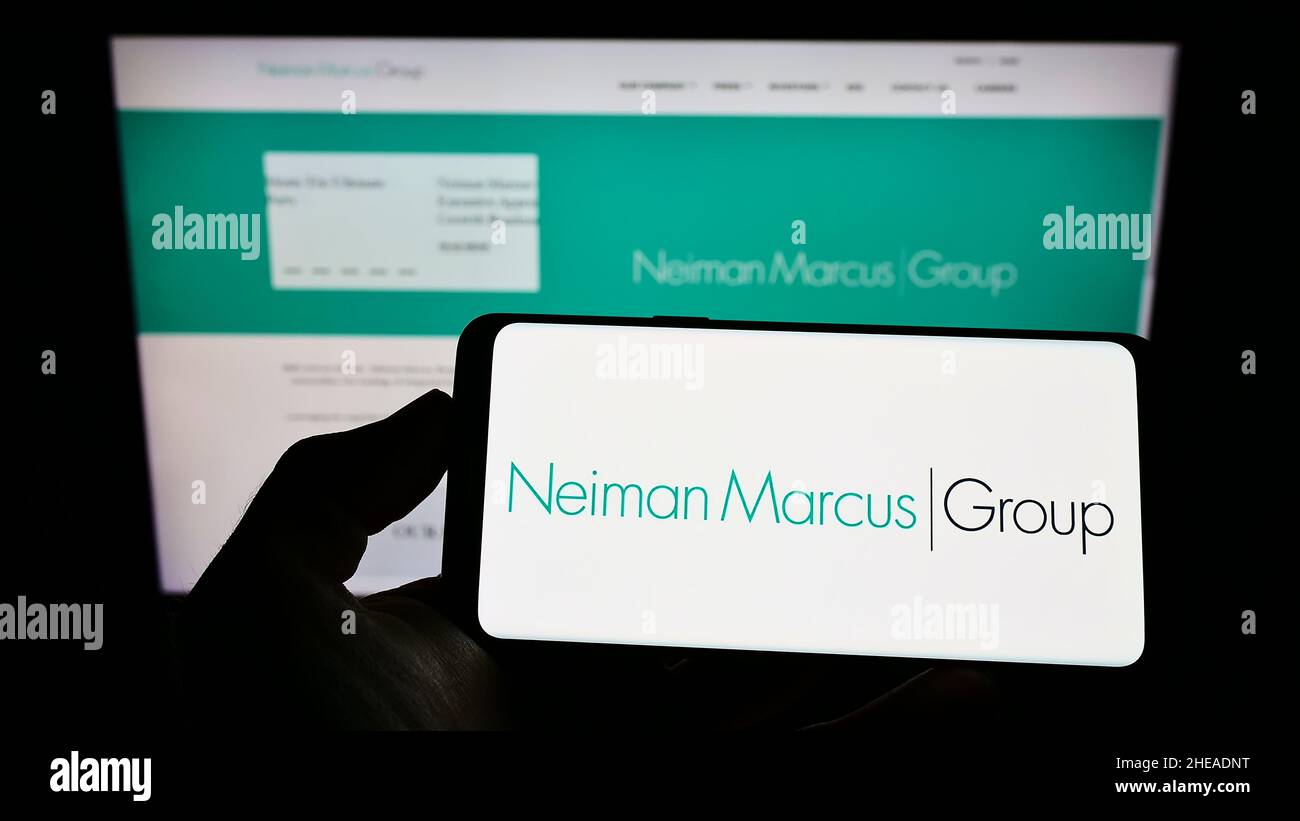 Personne tenant un téléphone portable avec le logo de la société de détail américaine Neiman Marcus Group Inc. À l'écran en face de la page Web d'affaires.Mise au point sur l'affichage du téléphone. Banque D'Images