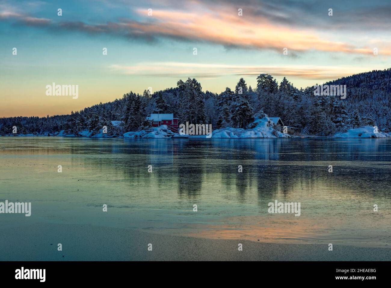 Le Vollsfjord recouvert de glace et le ciel coloré se reflète dans la glace.Paysage d'hiver avec îles, huttes, mer, rochers enneigés, ciel bleu,réflexion au coucher du soleil., Banque D'Images