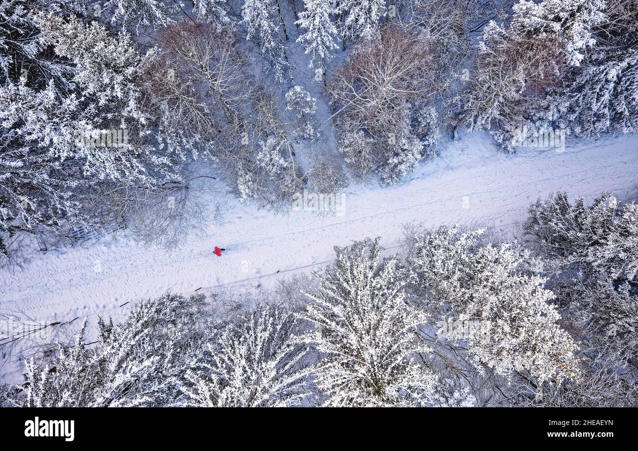 Vue aérienne en haut de la forêt enneigée avec route d'hiver et homme en veste rouge.Paysage de photographie de drone.Vue de dessus. Banque D'Images