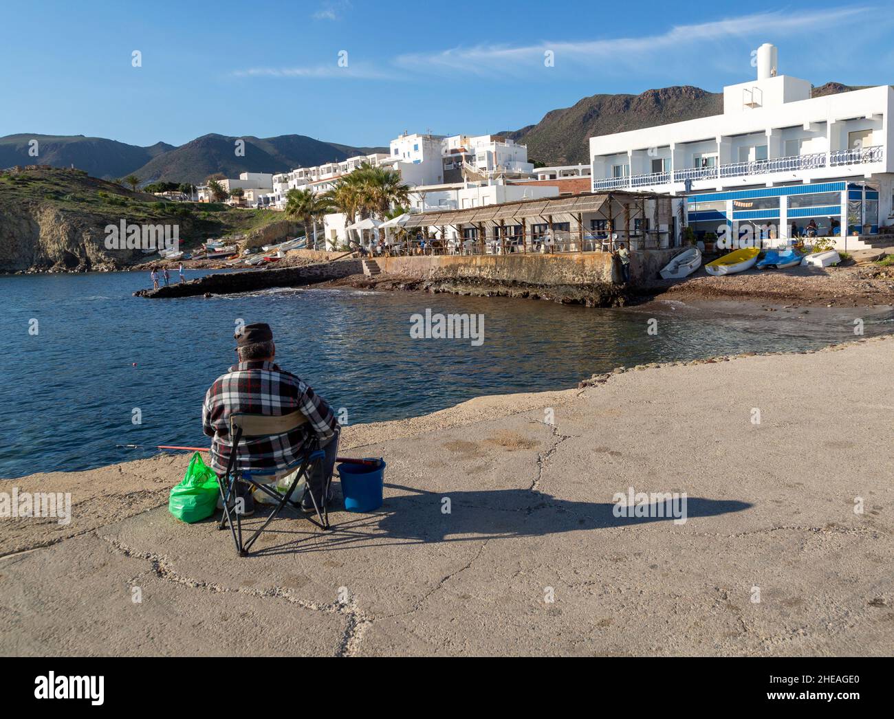 Homme pêche depuis la jetée, restaurant en bord de mer, hôtel et logement à Isleta del Moro, parc naturel de Cabo de Gata, Almeria, Espagne Banque D'Images