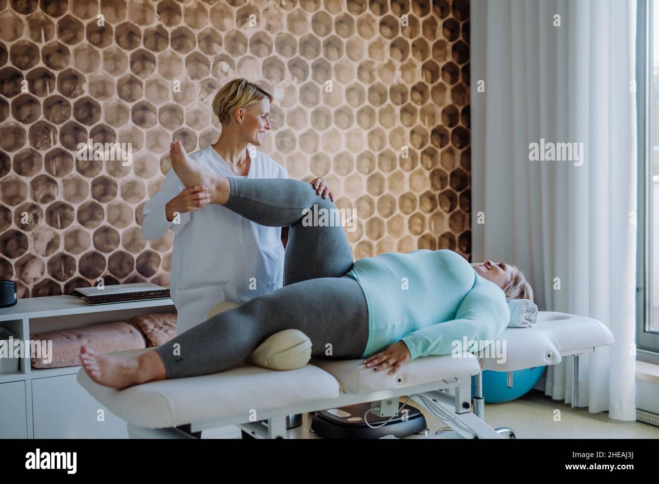Femme physiothérapeute adulte de taille moyenne s'exerçant avec une femme en surpoids à l'intérieur dans un centre de réadaptation Banque D'Images