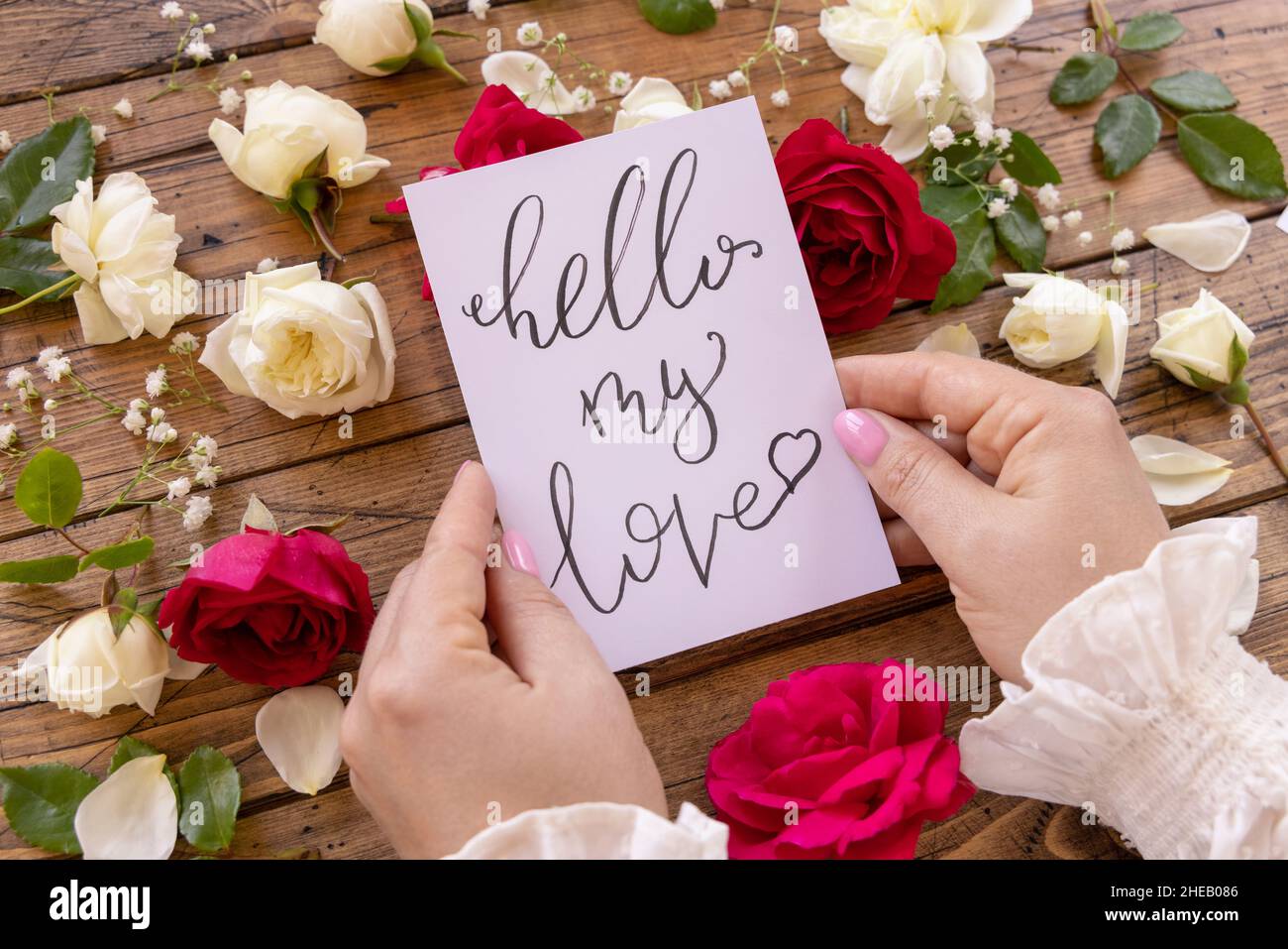 Mains avec carte manuscrite BONJOUR MON AMOUR entouré de roses rouges et crème gros plan sur une table en bois.Femminine déclaration romantique de l'amour près de fl Banque D'Images