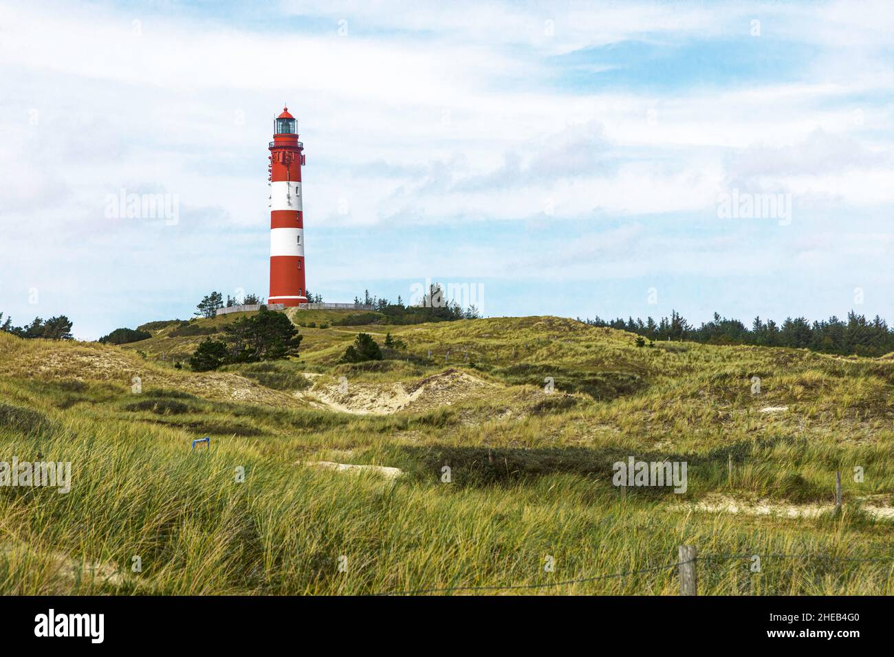 Grand bâtiment de phare rayé rouge et blanc sur une petite colline. Paysage côtier sablonneux avec végétation verte et sentiers. Jour d'été en mer Banque D'Images