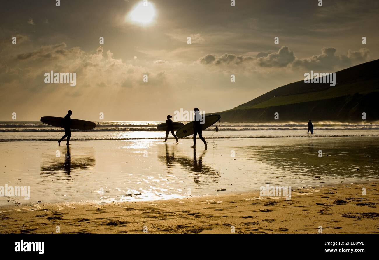 Vue panoramique de 3 Surfers silhouettés contre le soleil avec des reflets de plage sur la plage de Saunton Sands au nord de Devon Royaume-Uni. Banque D'Images