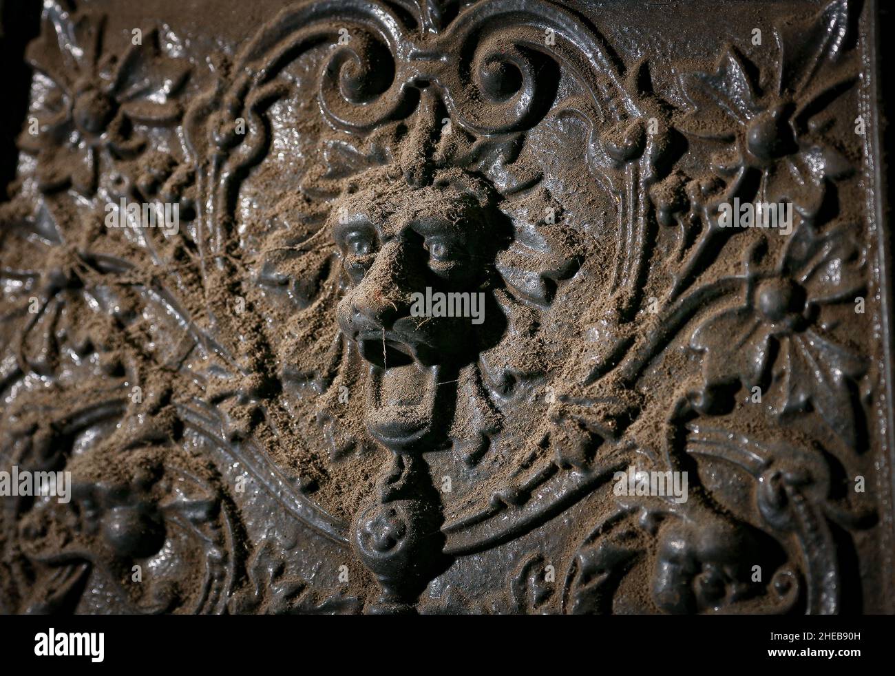 Un lion décoratif ornement tête avec des yeux piecing sur une ancienne cheminée en fonte trouvée dans une vieille maison avant le début des travaux de rénovation. Banque D'Images