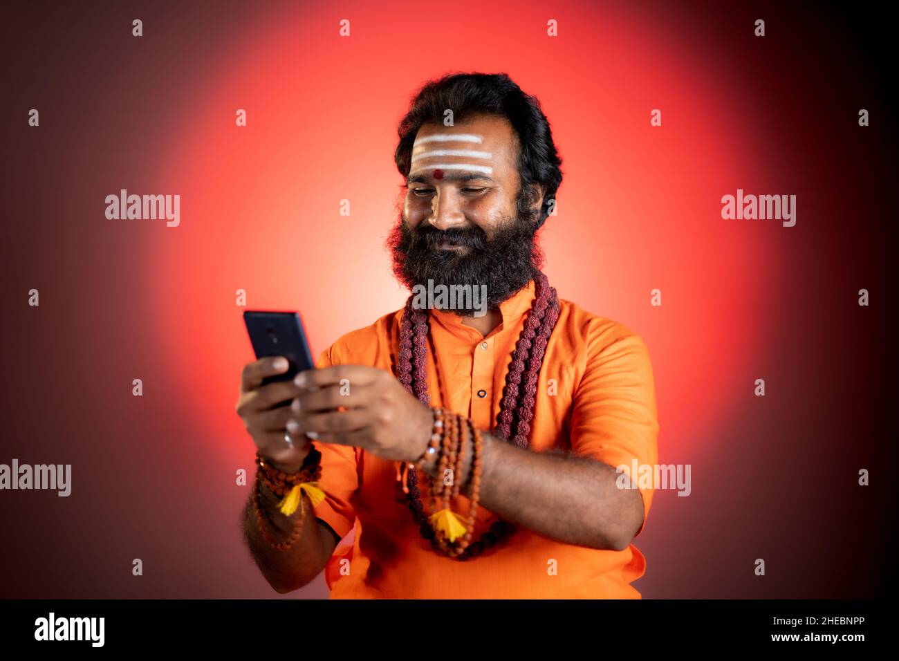 Dieu indien Saint homme occupé à utiliser les médias sociaux sur le téléphone mobile au monastère - concept de Mobile astrologue service , technologie et Internet. Banque D'Images