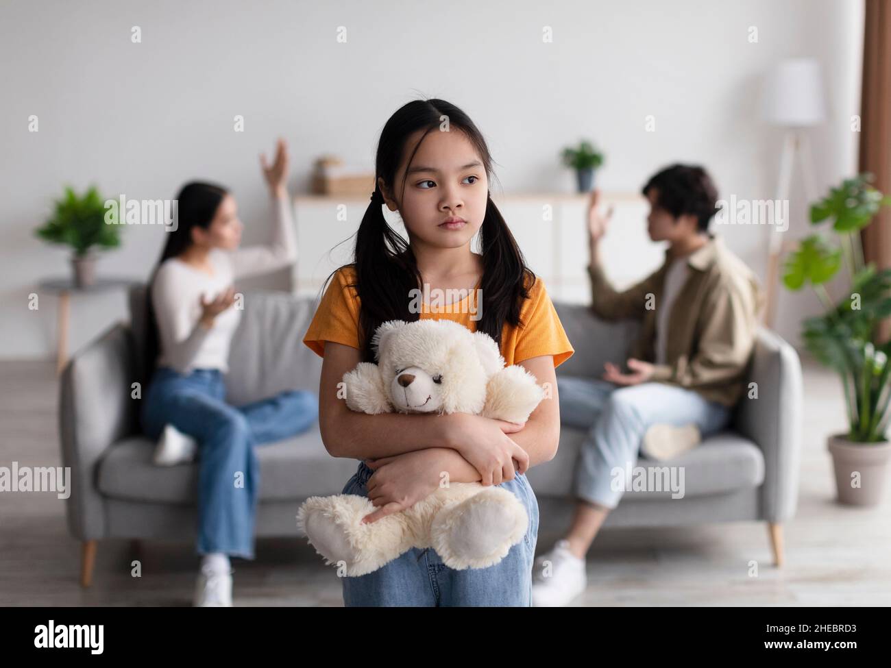 Solitaire triste chinoise jeune fille avec jouet souffre de scandale de parents, jeune asiatique dame et gars quarreling à la maison Banque D'Images