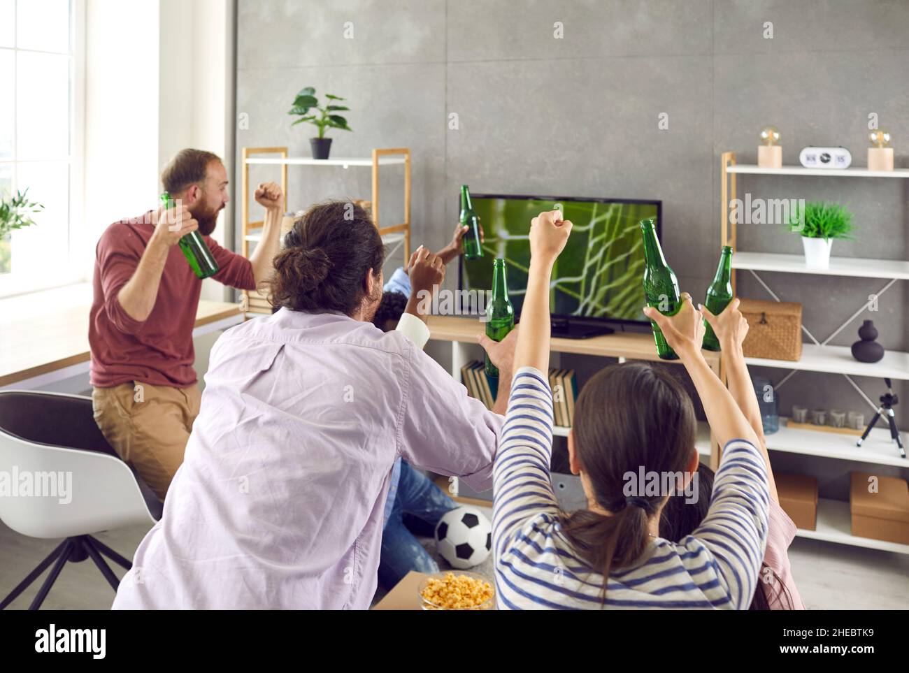 Un groupe d'amis adultes actifs regardent émotionnellement un match de football à la télévision à la maison. Banque D'Images