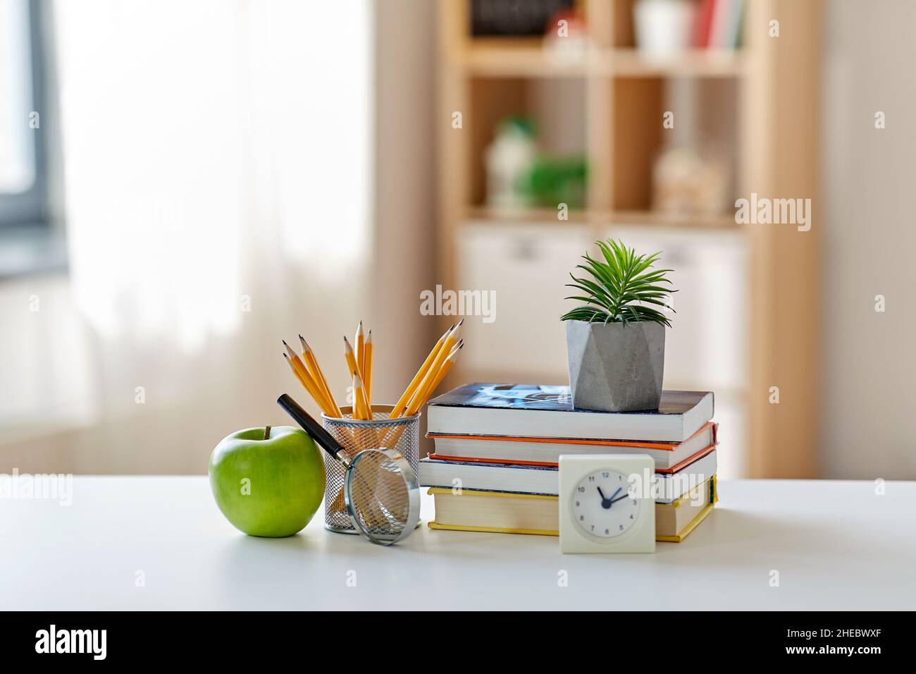 livres, loupe, crayons, pomme sur table à la maison Banque D'Images