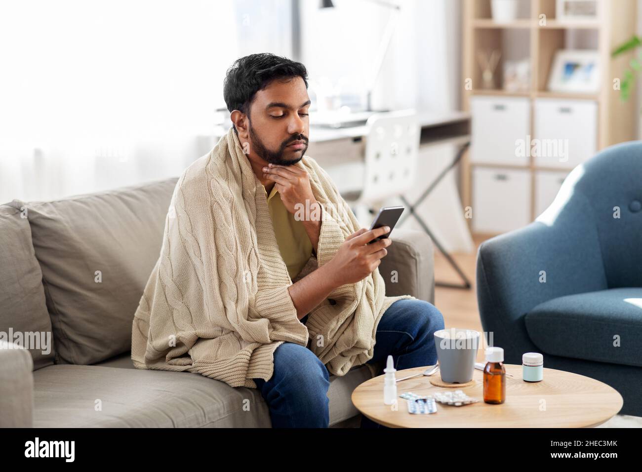 jeune homme malade en couverture avec smartphone à la maison Banque D'Images