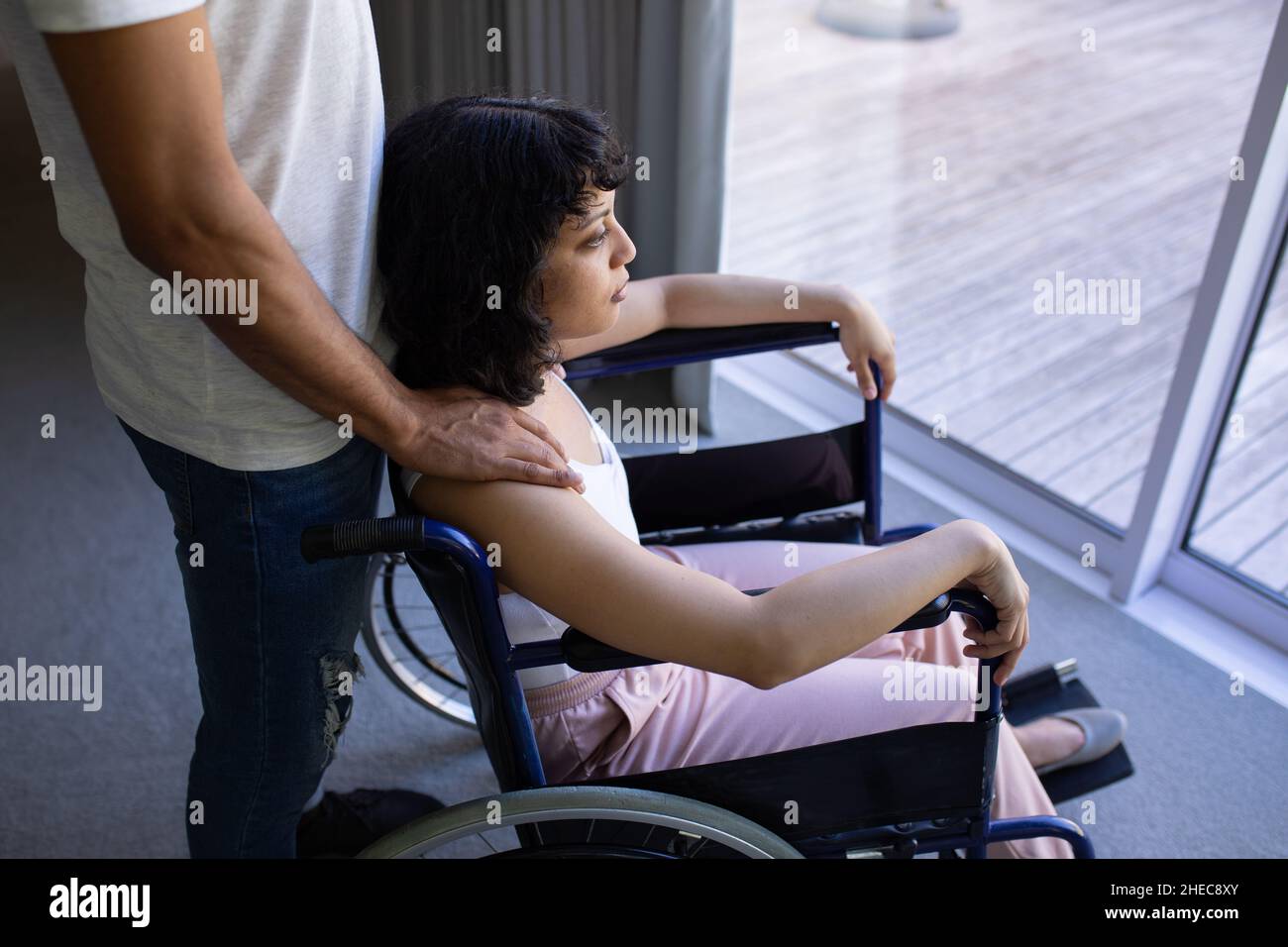 Section centrale d'un homme avec sa main sur l'épaule de sa femme handicapée en fauteuil roulant à la maison Banque D'Images