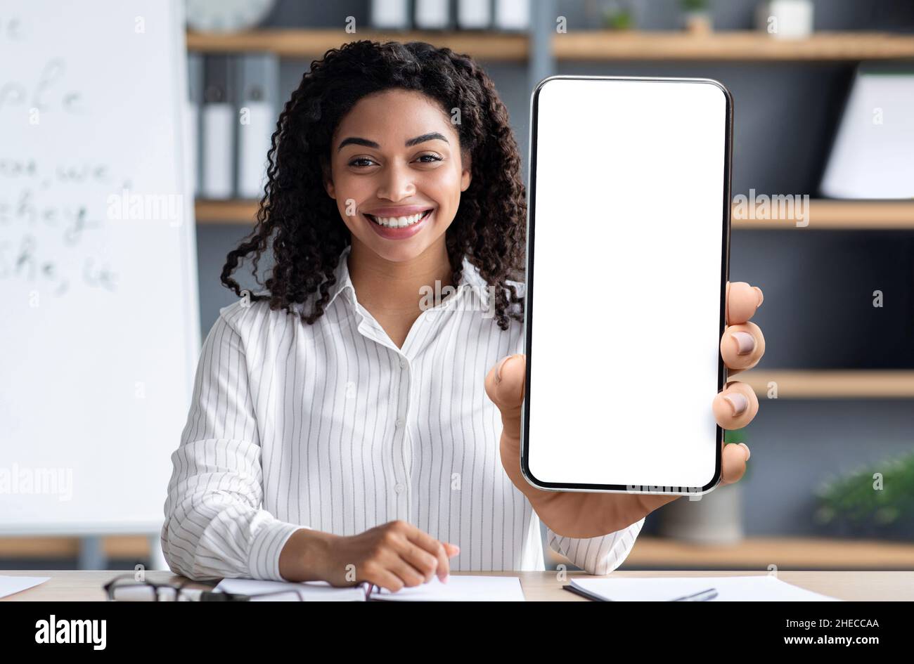 Concept d'apprentissage en ligne.Tutor noir souriant montrant un grand smartphone vierge à l'appareil photo Banque D'Images