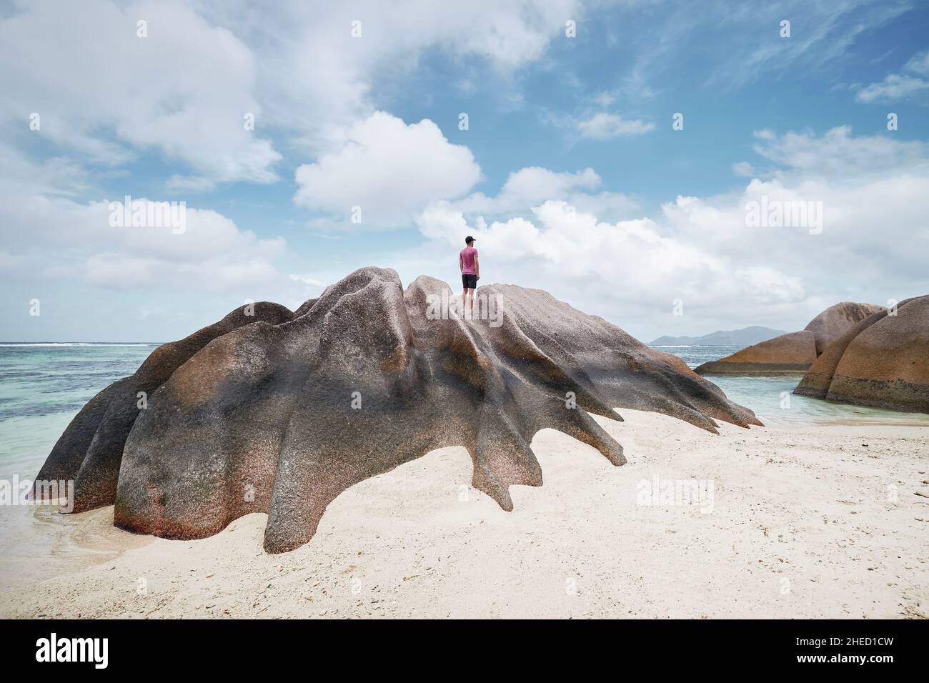 Homme debout sur le rocher et regardant la vue.Solitaire touriste appréciant le calme sur la plage idyllique aux Seychelles. Banque D'Images