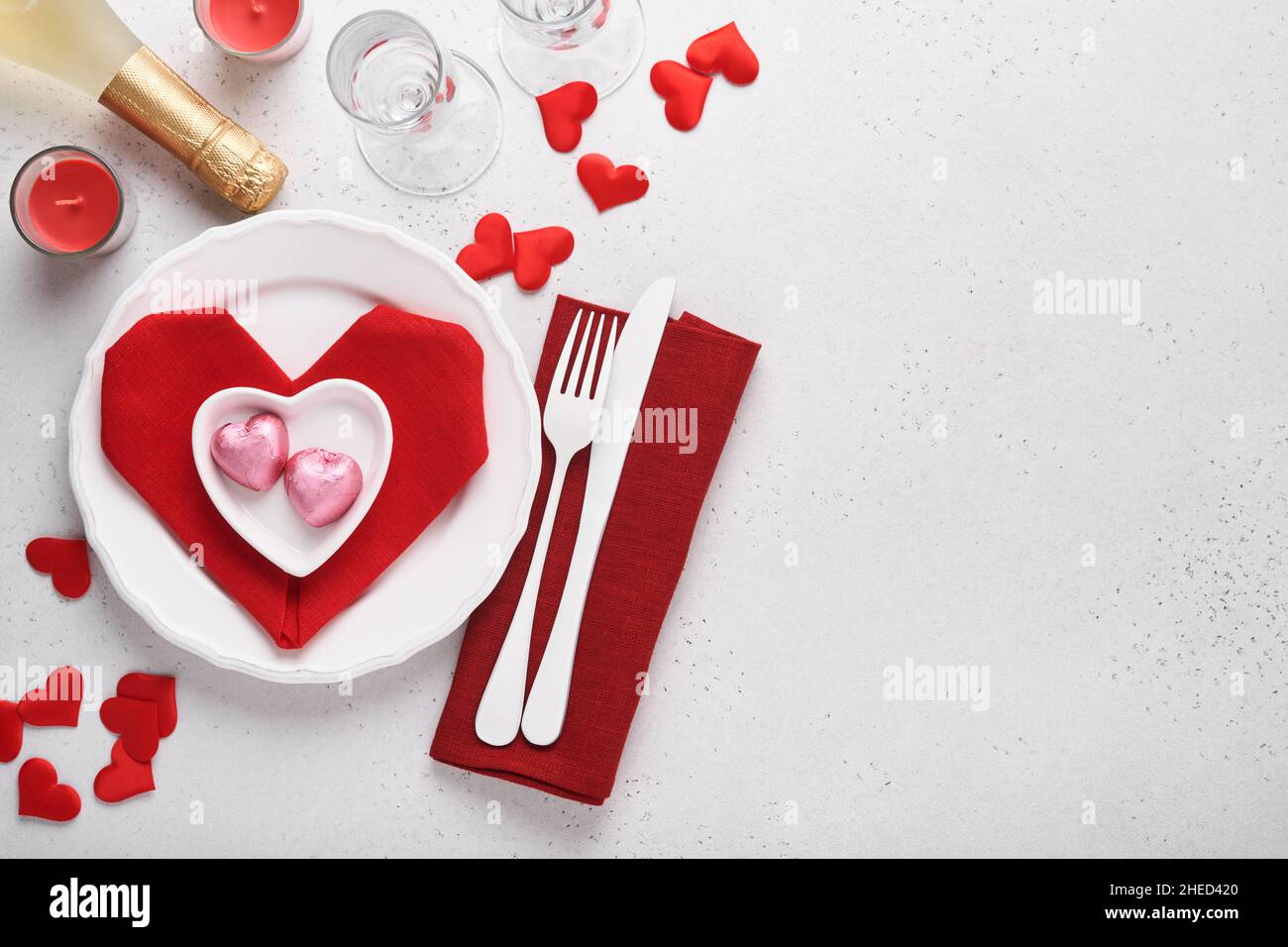 Table de jour de Valentinas couleur blanche avec argenterie blanche, serviette rouge pliée comme coeur, bougies, champagne, verres sur fond blanc pour greeti Banque D'Images