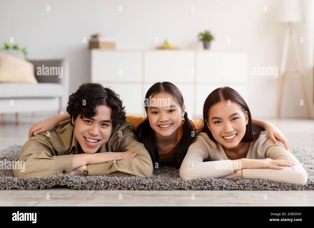 Souriant bonne femme du millénaire chinois, gars et fille de l'adolescence se reposant sur le sol dans le salon intérieur, regardez la caméra Banque D'Images