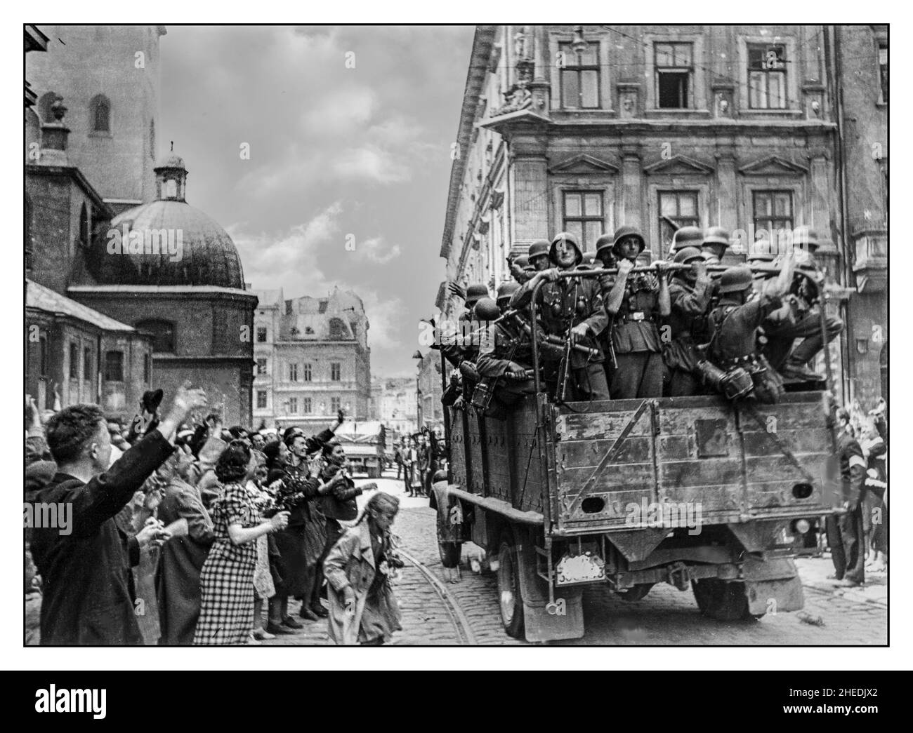 LVIV UKRAINE 1940s WW2 occupation de l'Allemagne nazie à Lviv Ukraine. Les civils accueillent l'armée allemande lorsqu'ils entrent dans la ville. Au premier plan, un camion militaire avec des soldats et des civils allemands, juste à côté de la cathédrale latine - l'une des plus anciennes églises de Lviv. Lviv est une ville de l'ouest de l'Ukraine, à environ 70 kilomètres de la frontière avec la Pologne Banque D'Images